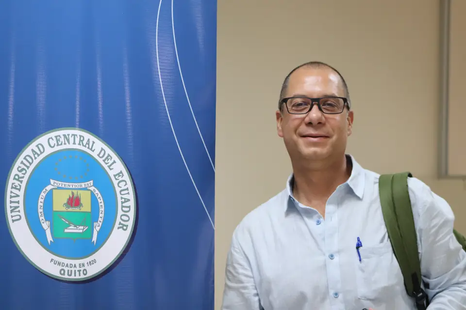 Participante junto al banner de la Universidad Central del Ecuador
